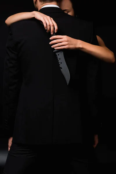 Vista parcial de la mujer peligrosa sosteniendo cuchillo detrás de la espalda del hombre aislado en negro - foto de stock