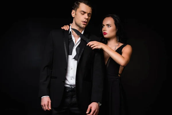 Dangerous woman in dress holding knife near neck of man in suit isolated on black — Stock Photo