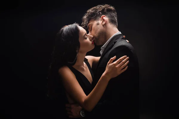 Sexy woman with red lips kissing with man in suit isolated on black — Stock Photo