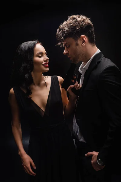 Dangerous woman smiling while holding gun near man in suit on black — Stock Photo