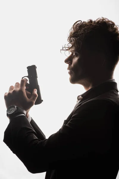 Вид сбоку кудрявого человека в костюме, держащего в руках пистолет, изолированный на белом — стоковое фото