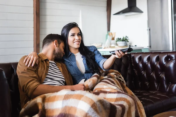 Lächelnde Frau umarmt Schulter eines schlafenden Mannes beim Fernsehen unter warmer Decke — Stockfoto