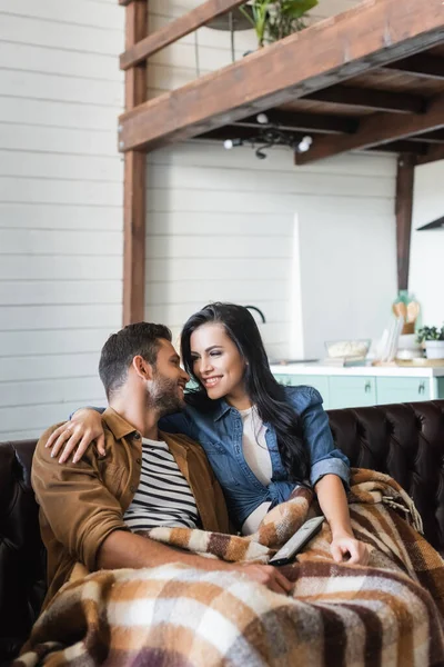 Homem feliz e mulher olhando um para o outro enquanto assiste tv sob cobertor acolhedor — Fotografia de Stock