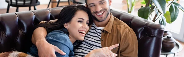 Lachende Frau, die mit dem Finger zeigt, während sie mit ihrem fröhlichen Freund fernsieht, Banner — Stockfoto