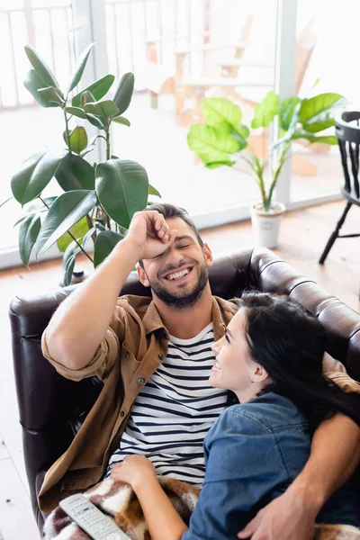 Uomo allegro ridendo con gli occhi chiusi mentre riposa con la ragazza sul divano di pelle — Foto stock