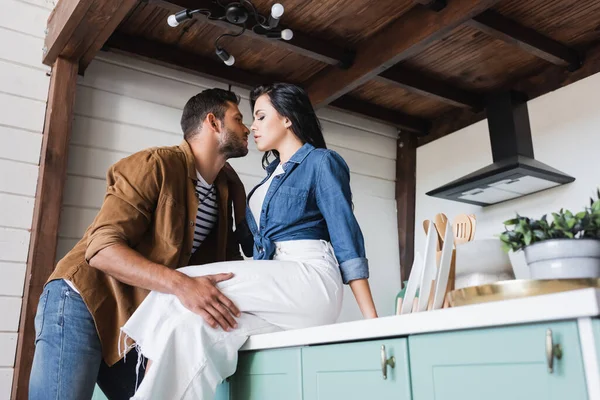 Молодий чоловік торкається чуттєвої жінки, сидячи на кухонній стійці в стильному повсякденному одязі — стокове фото