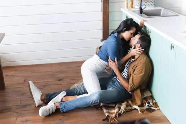 Sedutor mulher beijando jovem sentado no chão na cozinha — Fotografia de Stock