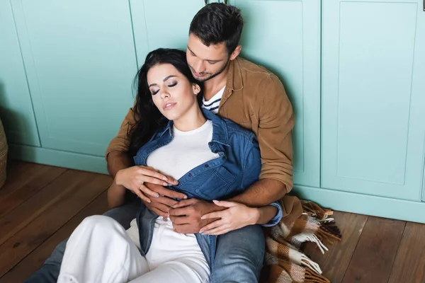 Young man and woman in stylish casual clothes hugging while sitting on floor — Stock Photo