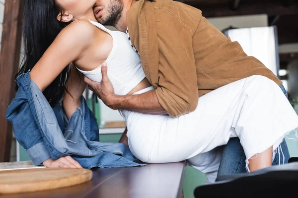 Cropped view of man embracing sexy woman sitting on table — Stock Photo