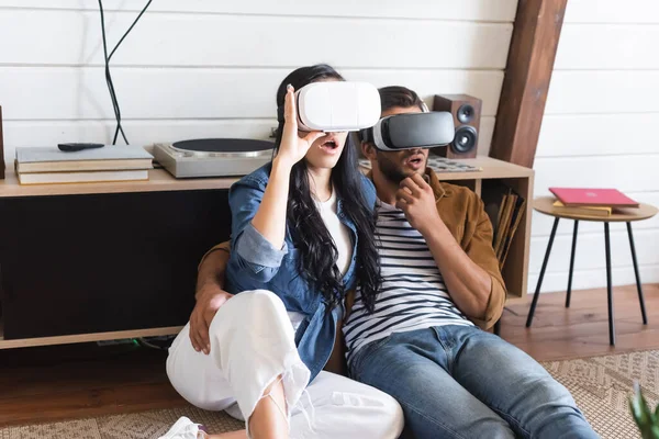 Amazed man hugging girlfriend while gaming in vr headsets together on floor — Stock Photo