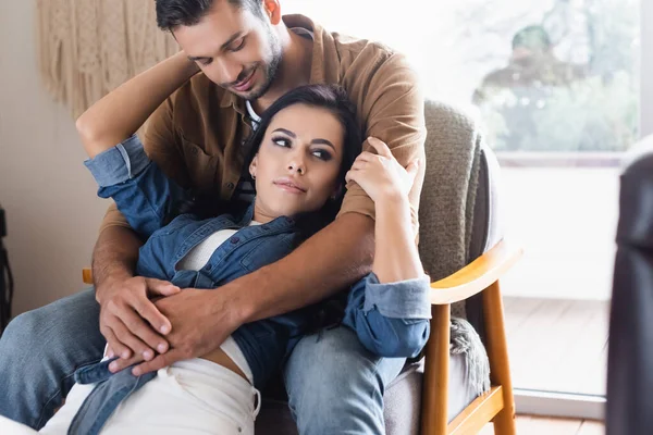 Glücklicher Mann sitzt im Sessel und umarmt Freundin zu Hause — Stockfoto