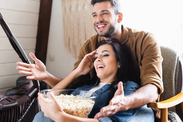 Excited man pointing with hands while watching tv with girlfriend holding bowl of popcorn — Stock Photo