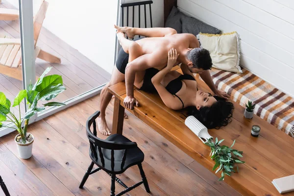 Vista ad alto angolo di uomo muscoloso senza camicia che fa l'amore con la donna appassionata in biancheria intima nera sul tavolo di legno — Foto stock