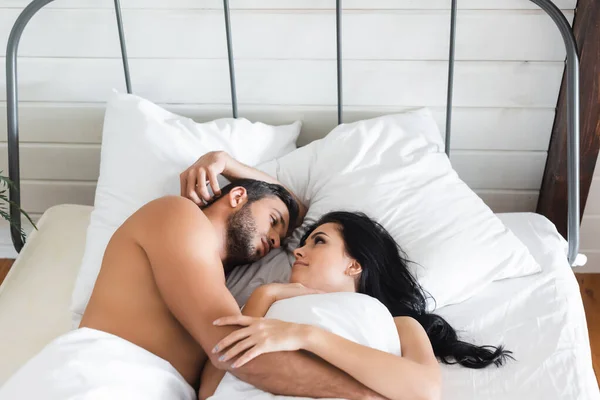 Молода пара дивиться один на одного, лежачи в ліжку під ковдрою — стокове фото