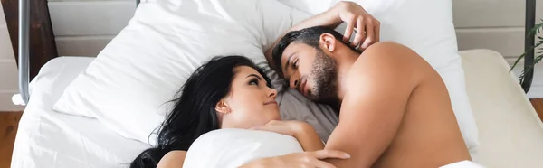 Jóvenes amantes tumbados en la cama debajo de la manta y mirándose unos a otros, pancarta - foto de stock