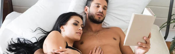 Uomo senza maglietta con bruna fidanzata lettura libro mentre si trova a letto, banner — Foto stock