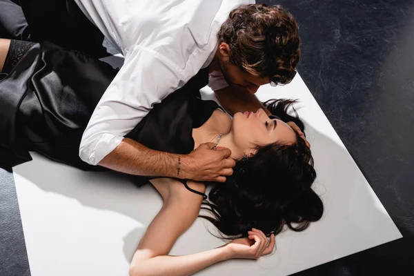Vista aerea di uomo in camicia bianca toccare collana sulla donna sexy sdraiato sul pavimento in bianco e nero — Foto stock