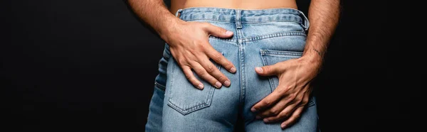 Recortado vista de la mujer en jeans cerca de hombre abrazando sus nalgas aislado en negro, bandera - foto de stock