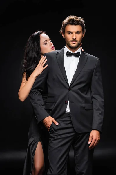 Passionate brunette woman seducing confident man in formal wear on black — Stock Photo