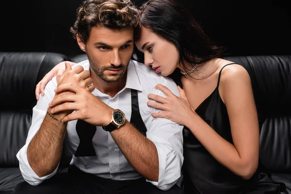 Sensual woman leaning on shoulder of elegant man on leather sofa isolated on black — Stock Photo