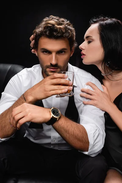 Femme passionnée séduire homme tenant verre de whisky isolé sur noir — Photo de stock