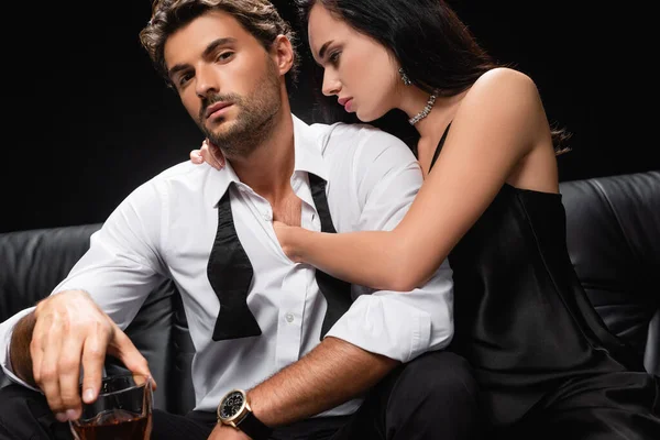 Sensual brunette woman embracing man holding glass of whiskey isolated on black — Stock Photo