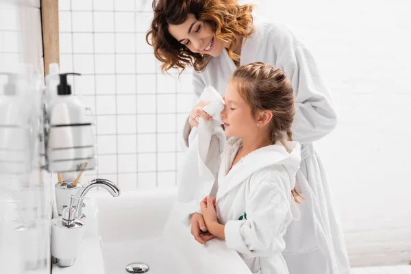 Sonriente madre secando la cara de la hija con toalla en el baño - foto de stock