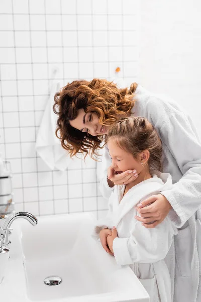Усміхнена жінка обіймає дитину біля раковини в сучасній ванній — стокове фото