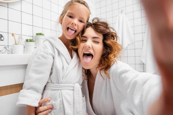Mother and child sticking out tongues in bathroom — Stock Photo