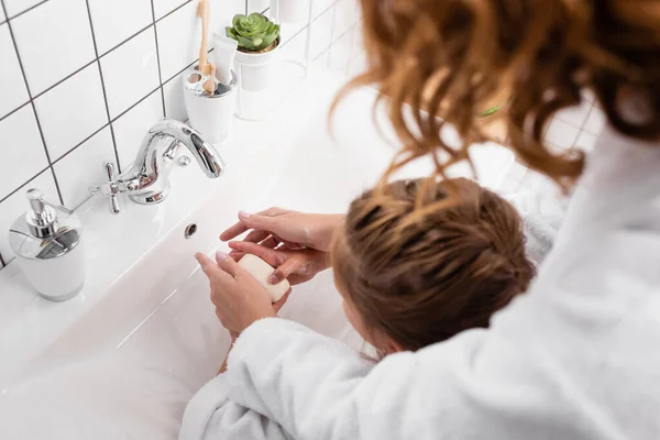 Vista aerea del sapone nelle mani di madre e bambino in primo piano sfocato in bagno — Foto stock