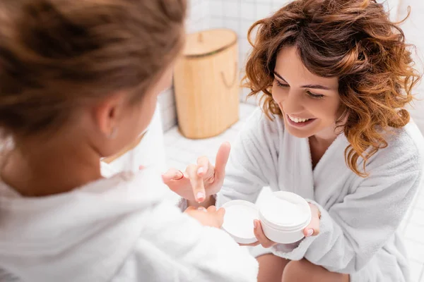 Mãe alegre que aplica a nata cosmética à mão da filha no primeiro plano borrado — Fotografia de Stock