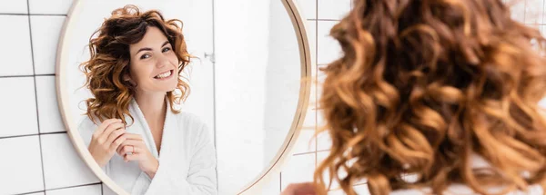 Curly mulher olhando para o espelho em primeiro plano desfocado no banheiro, banner — Fotografia de Stock