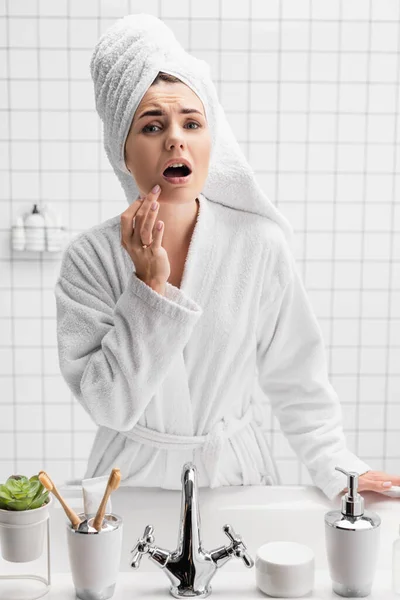 Mulher preocupada em toalha e roupão de banho tocando queixo — Fotografia de Stock