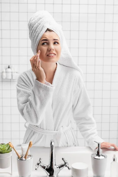 Mujer disgustada en toalla tocando mejilla en el baño - foto de stock