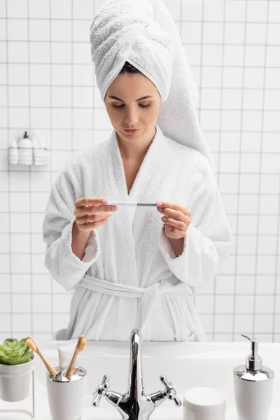 Femme tenant test de grossesse près de l'évier dans la salle de bain — Photo de stock