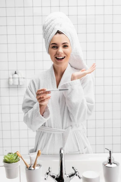 Mujer alegre en albornoz celebración de la prueba de embarazo en el baño - foto de stock