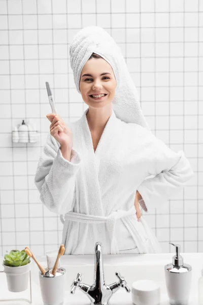 Mulher sorridente em toalha mostrando teste de gravidez no banheiro — Fotografia de Stock