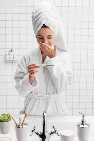 Donna stupita in asciugamano e accappatoio che tiene test di gravidanza in bagno — Foto stock