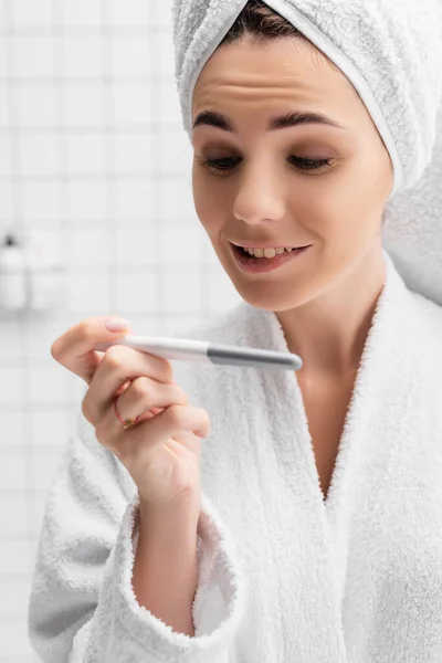 Smiling woman in bathrobe looking at pregnancy test on blurred foreground — Stock Photo