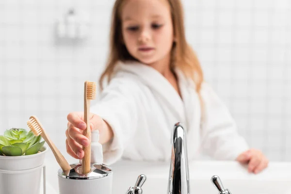 Зубная щетка в руке девушки на размытом фоне в ванной комнате — стоковое фото