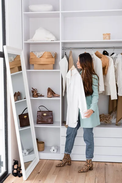 Young woman holding shirt near mirror in wardrobe — Stock Photo