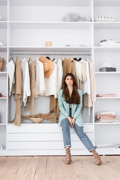 Young woman looking at camera while sitting on shelf in wardrobe — Stock Photo