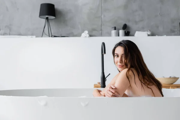 Brünette Frau schaut Kamera in Badewanne zu Hause an — Stockfoto