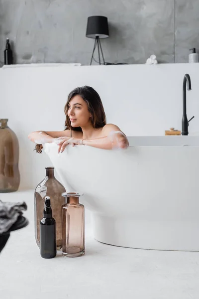 Jeune femme couchée dans la baignoire près des bouteilles décoratives — Photo de stock