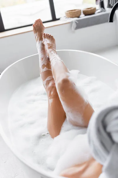 Beine einer jungen Frau in Schaumstoff in Badewanne auf verschwommenem Vordergrund — Stockfoto
