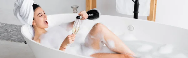 Femme gaie versant du champagne dans un verre dans une baignoire avec mousse, bannière — Photo de stock