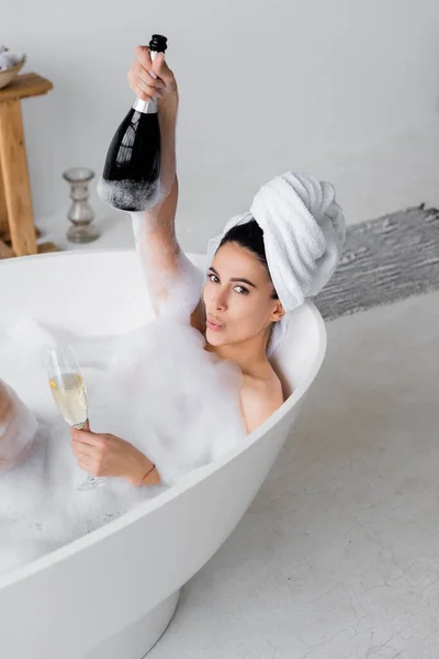 Молода жінка з шампанським дивиться на камеру у ванній з пілінгом — стокове фото