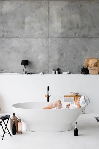 Jeune femme buvant du champagne tout en prenant un bain avec mousse — Photo de stock