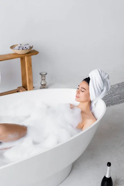 Femme prenant un bain avec mousse près de la bouteille de champagne — Photo de stock