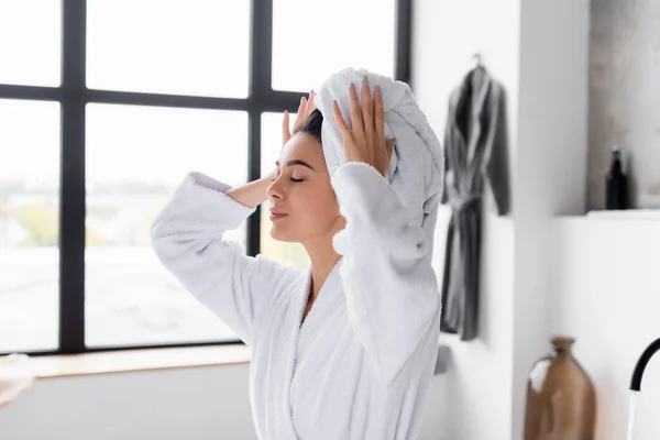 Woman in bathrobe holding white towel on head in bathroom — Stock Photo